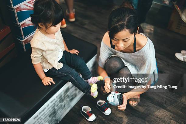 young mom helping toddler fitting with new shoes - シューズショップ ストックフォトと画像