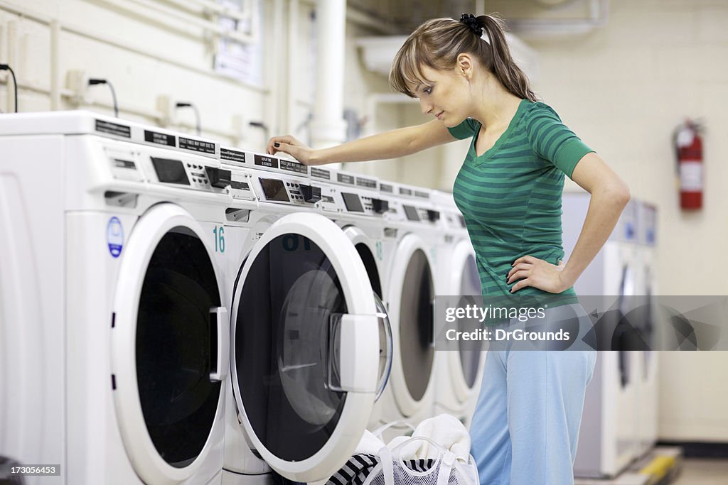 Woman in laundromat loading clothes into washing machine