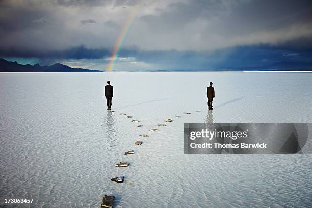 two men on forked pathway in water under rainbow - stepping stone stock-fotos und bilder