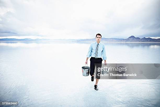 businessman carrying buckets through shallow water - hochgekrempelte hose stock-fotos und bilder