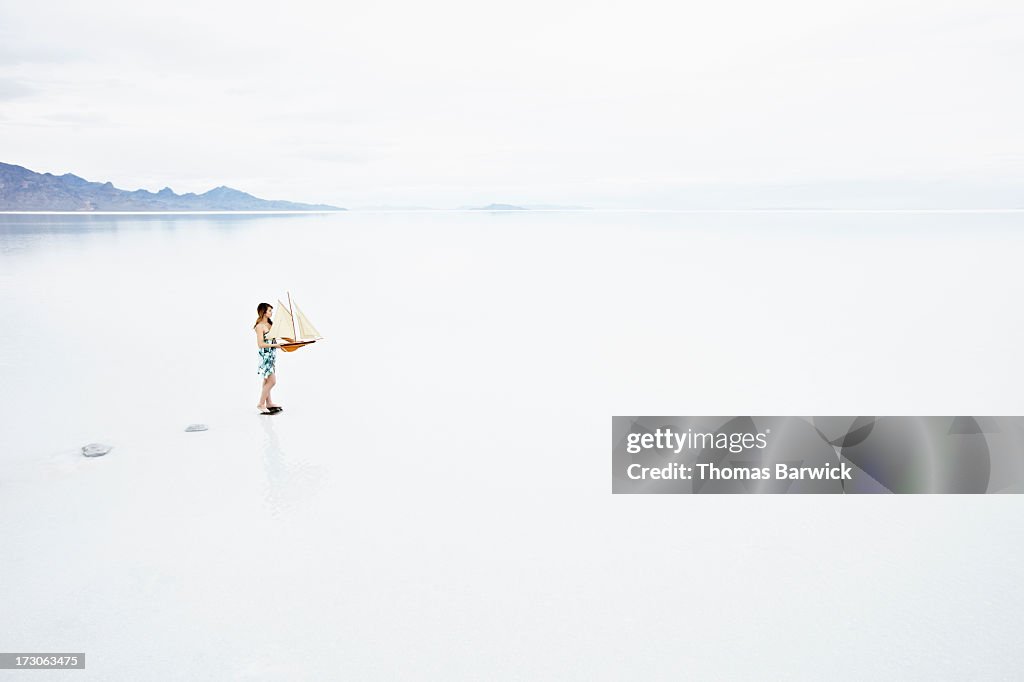 Woman on path in lake holding model sailboat