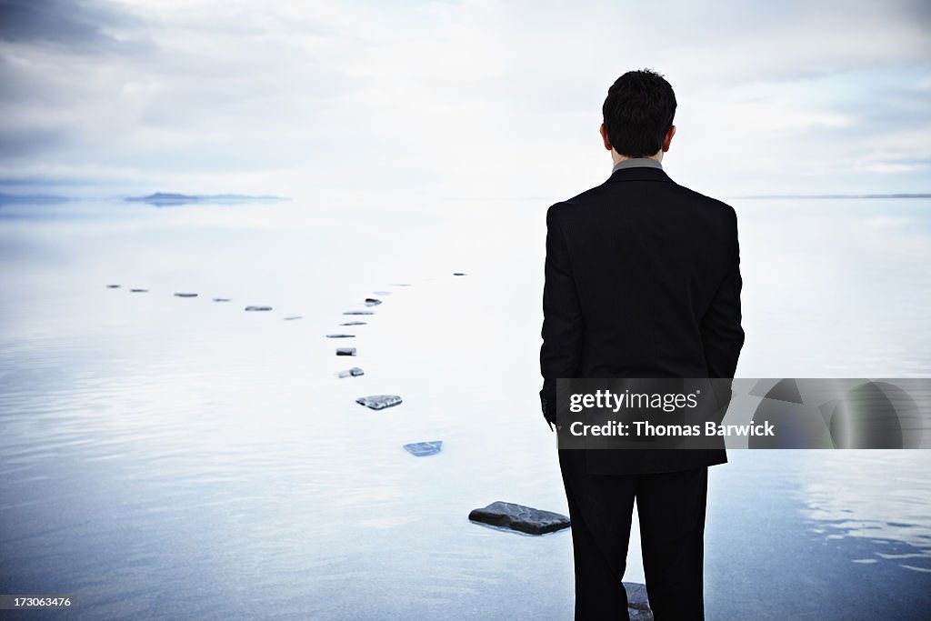 Businessman standing on stone pathway in water