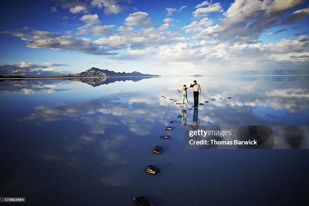 Man helping woman balance on stone pathway in lake