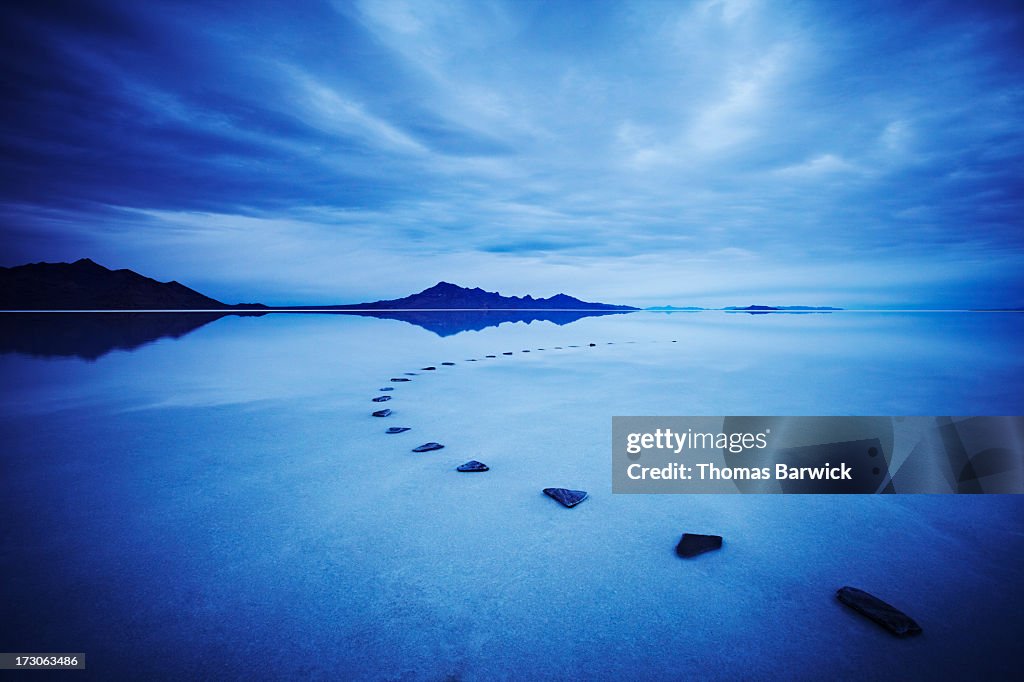 Curved stone pathway in calm lake at sunrise