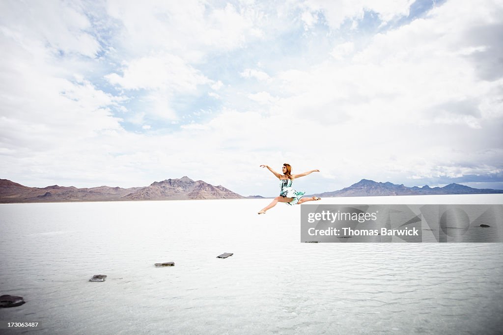 Woman leaping over gap in stone pathway on lake