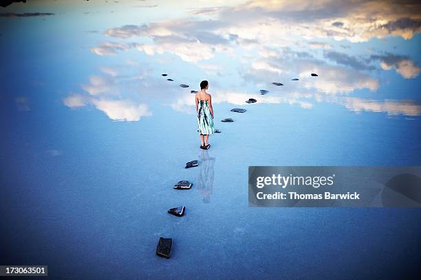 woman standing at fork in stone pathway in lake - dreamers stock-fotos und bilder