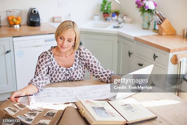 smiling woman at table with old photographs and genealogical tree - photo album stock pictures, royalty-free photos & images
