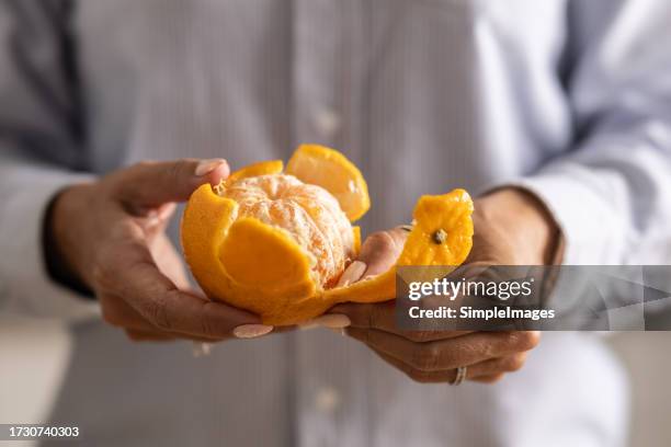 close-up of a woman's hands peeling a tangerine. - tangerine stock pictures, royalty-free photos & images