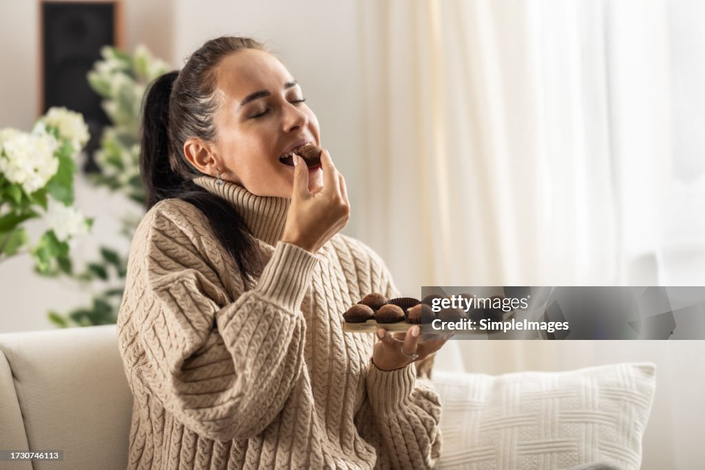 A young woman couldn't resist the sweet temptation to eat chocolate candies and enjoys them with her eyes closed.