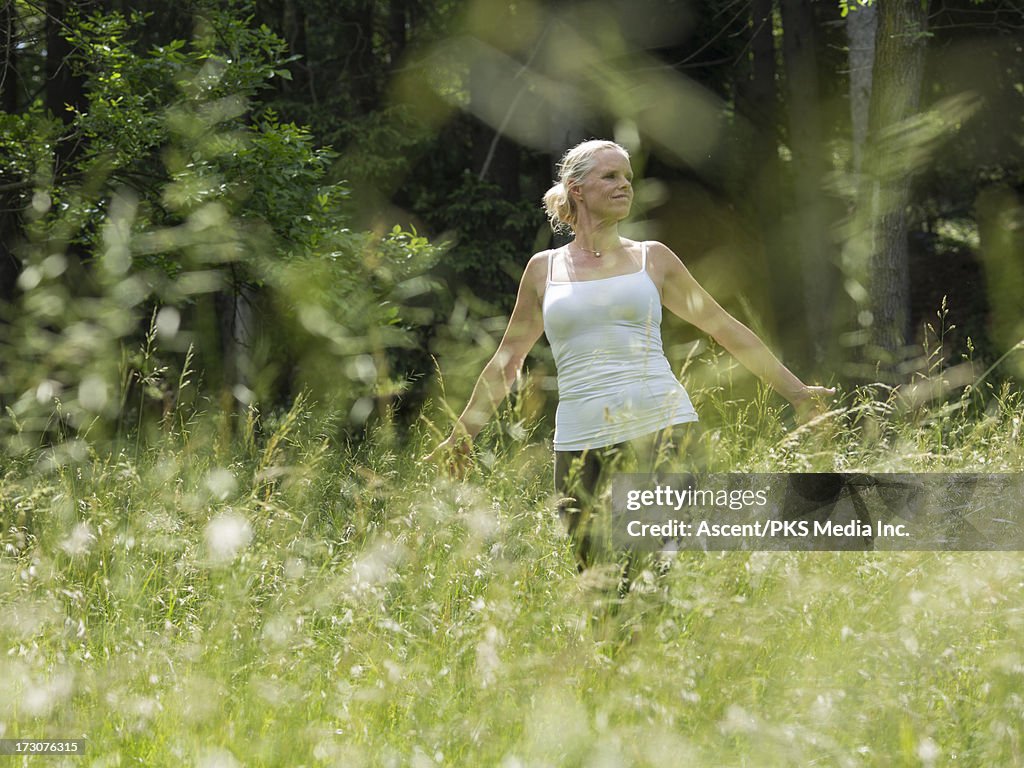 Woman walks through field of fresh grasses, forest