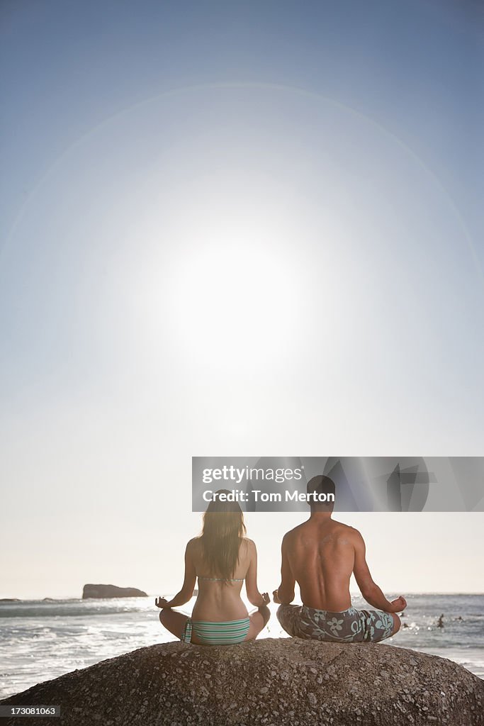 Couple meditating on rock near ocean