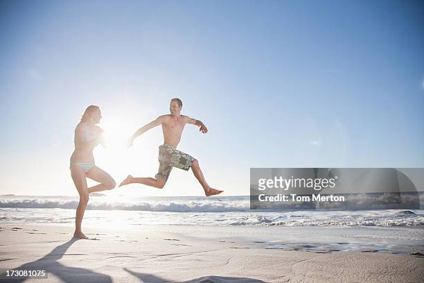 spielerische paar laufen am strand - mann freudensprung sonne vorderansicht leger stock-fotos und bilder