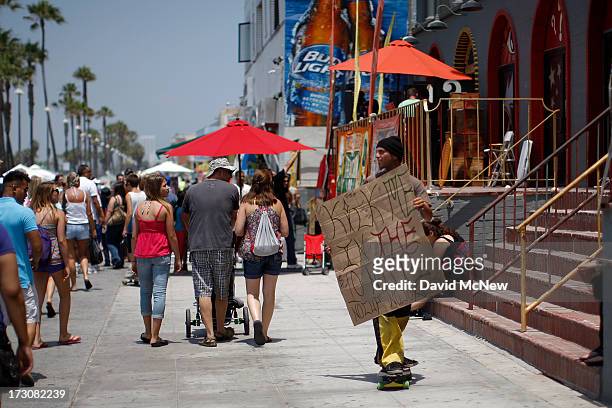 Man on a skateboard advertises his trade, getting paid to get kicked in the groin, on Independence Day weekend at Venice Beach on July 6, 2013 in...