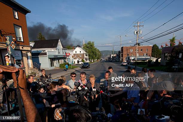 Smoke rises in the background as Quebec Prime Minister Pauline Marois speaks to reporters after a freight train loaded with oil derailed in Lac...
