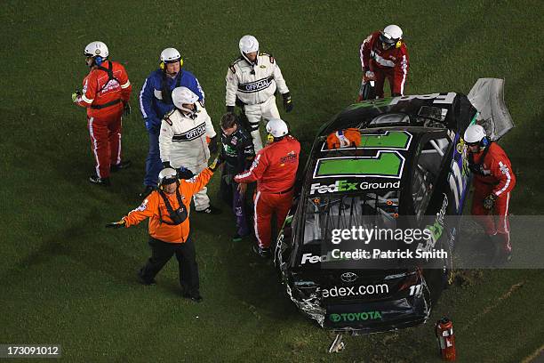 Denny Hamlin, driver of the FedEx Ground Toyota, is assisted by safety workers after a crash during the NASCAR Sprint Cup Series Coke Zero 400 at...