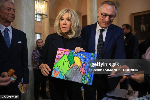 French President's wife Brigitte Macron holds a child's drawing reading "Thank You" next to former minister and President of Solidarite Defense...