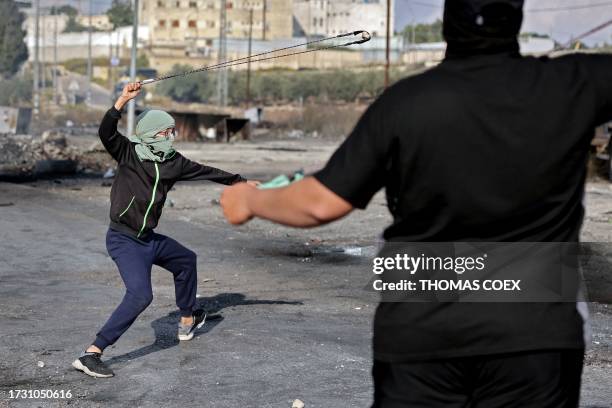 Palestinians use slingshots to throw stones towards Israeli soldiers during a demonstration in Ramallah, in the occupied West Bank on October 18...