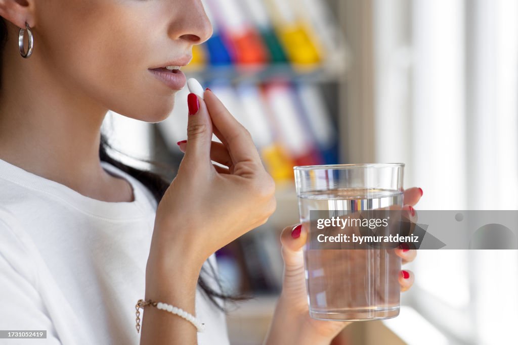 Donna che prende la compressa con un bicchiere di acqua fresca.
