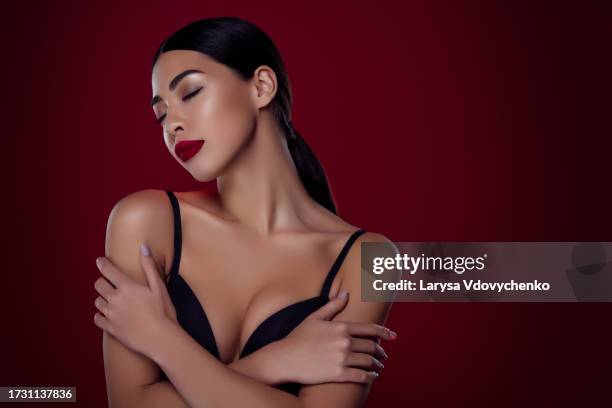 photo of lovely asian lady femme fatale closed eyes black bra hug self shoulders off isolated dark red color background - femme glamour stock pictures, royalty-free photos & images