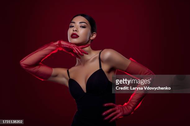 photo of asian young woman femme fatale touch chin gloves sensual self shoulders off isolated dark red color background - femme glamour stock pictures, royalty-free photos & images