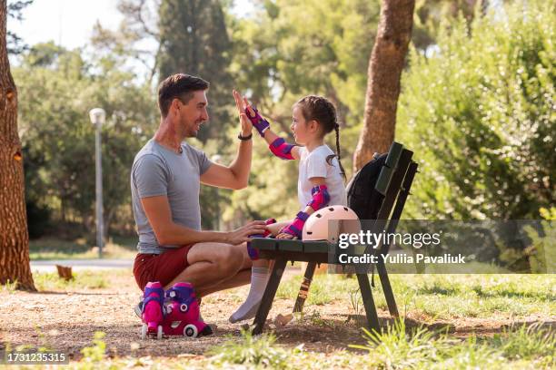 young father helps daughter put on sports protection for roller skating. man gives high five to girl - first half sport stock-fotos und bilder