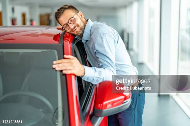 happy man embracing a car in a showroom. - falling in love stock pictures, royalty-free photos & images