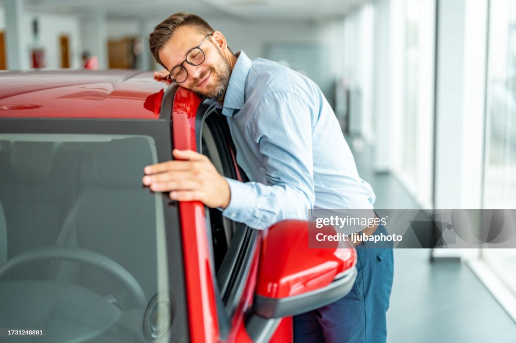 Happy man embracing a car in a showroom.