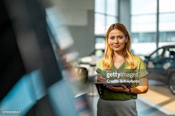 professional car dealer posing proudly at auto showroom, smiling to the camera, - car salesperson stock pictures, royalty-free photos & images