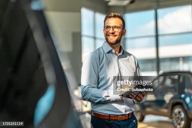 handsome male car salesman working in the showroom - salesman stock pictures, royalty-free photos & images