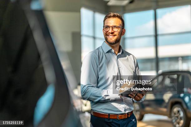 handsome male car salesman working in the showroom - car salesman stock pictures, royalty-free photos & images