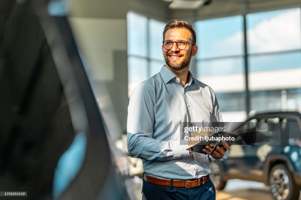 Handsome male car salesman working in the showroom