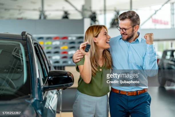 couple s’étreignant et souriant dans une nouvelle salle d’exposition de voitures - vehicle key photos et images de collection