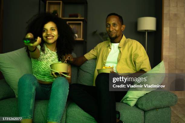 a young couple watching television while eating take-out food at home - zapping stock pictures, royalty-free photos & images