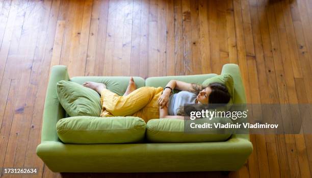 high angle shot of a woman comfortably lying on a sofa - hands on tummy stock pictures, royalty-free photos & images