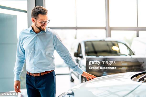 homme regardant la voiture tout en se tenant dans la salle d’exposition du concessionnaire - show room photos et images de collection