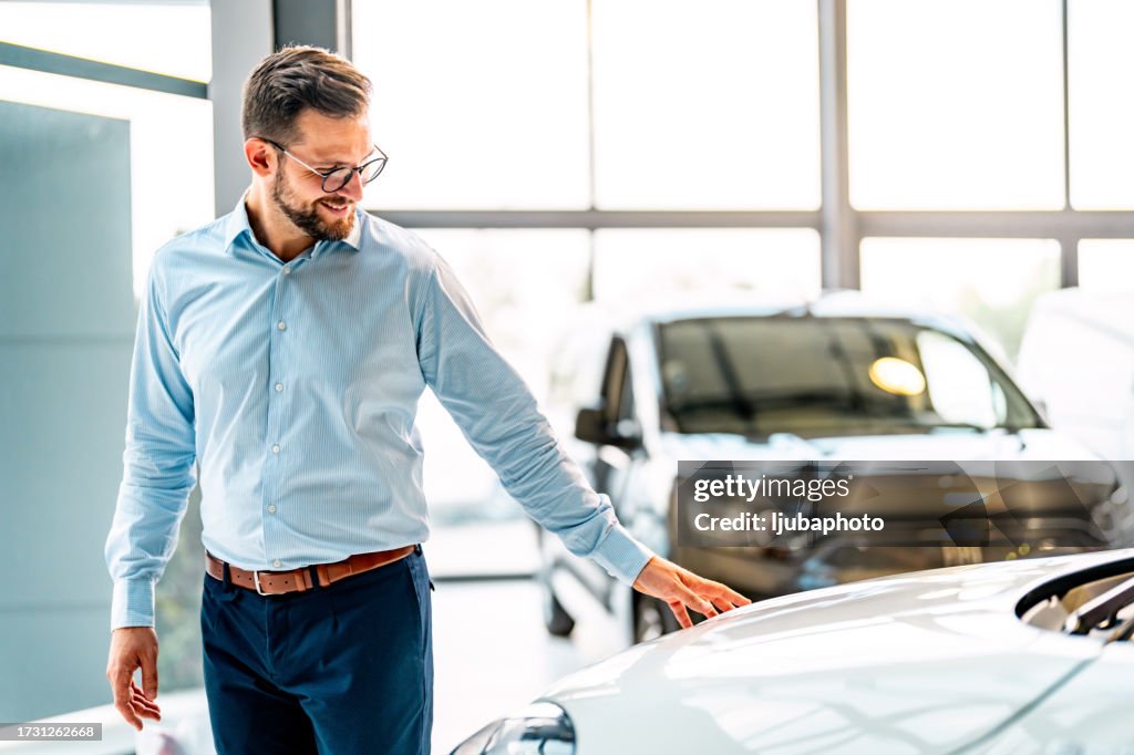 Man Looking At Car While Standing In Dealership Showroom