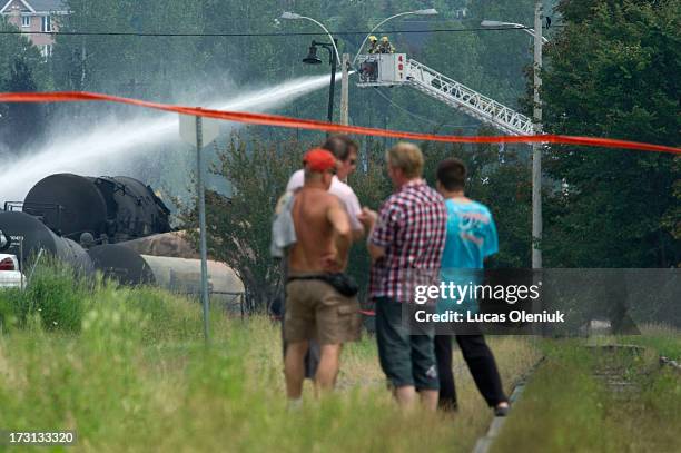 Towns people stand on the tracks leading to the derailed train in Lac-MÈgantic Sunday afternoon as firefighters continue to douse the smouldering...