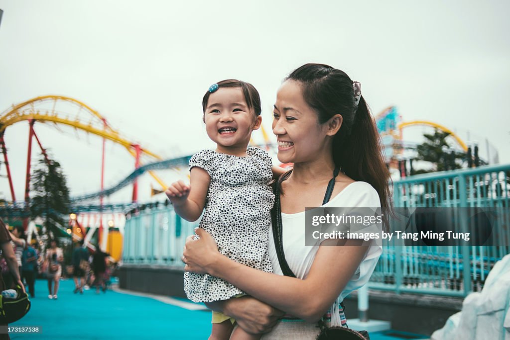 Mom holding toddler in amusement park joyfully