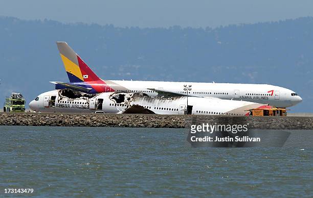 An Asiana Airlines flight enroute to Korea, a Boeing 777, taxis by the wreckage of Asiana Airlines flight 214 as it sits on runway 28L at San...
