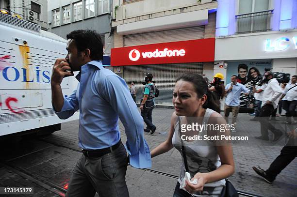 Pedestrians wince from tear gas beside a water cannon, as Turkish police battle anti-government protestors along the Istiklal shopping street near...