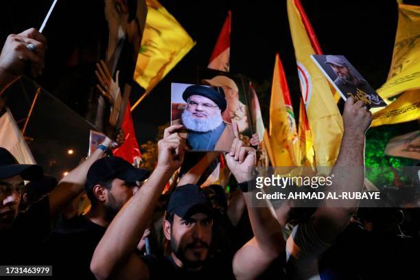 Iraqis hold portait of Lebanon's Hezbollah chief Hassan Nasrallah and shout slogans during a demonstration near the suspension bridge leading to...