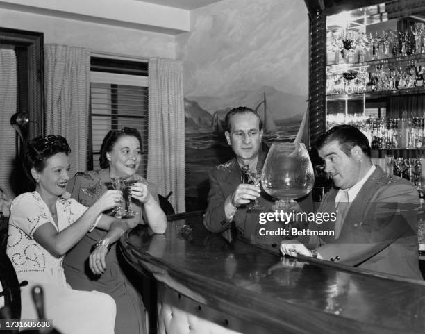 Lou Costello raising an oversized brandy glass as he joins comedy partner Bud Abbott and their respective wives Anne and Betty in a celebratory...