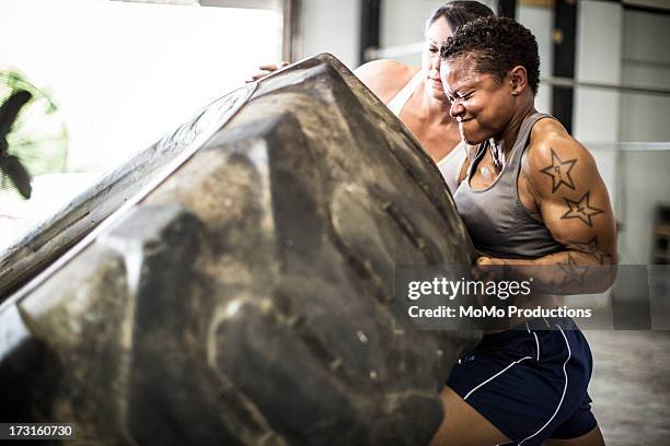 women doing tire-flip exercise - hartnäckigkeit stock-fotos und bilder