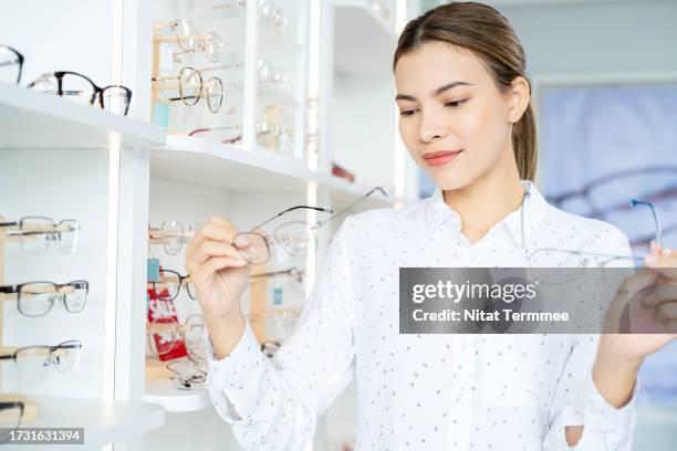 choosing the best glasses frames for a design that best suits your personality. a female customer at the optician store while choosing new pair of eye glasses from display shelf. - personalized picture frames stockfoto's en -beelden