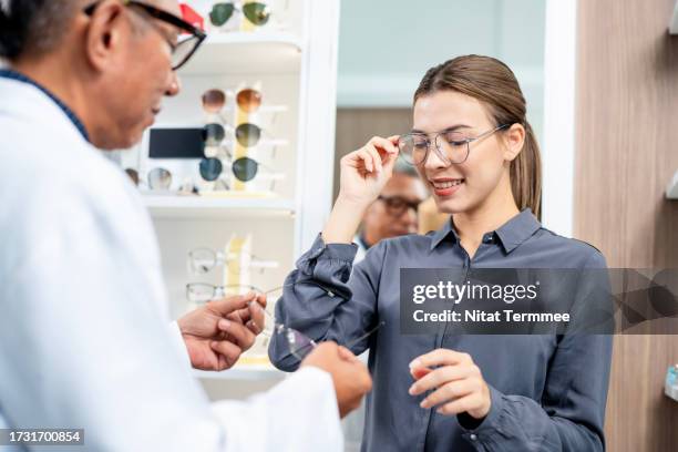 wear your glasses with confidence and embrace a more active lifestyle. a senior male optometrist is consulting with a young woman customer to try new glasses in front of a display cabinet at the optician's shop. - personalized stock pictures, royalty-free photos & images