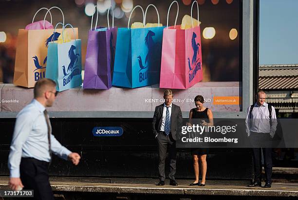 Commuters and rail travelers stand near an advertising billboard operated by JCDecaux SA, as they wait for a passenger train at Clapham Junction...