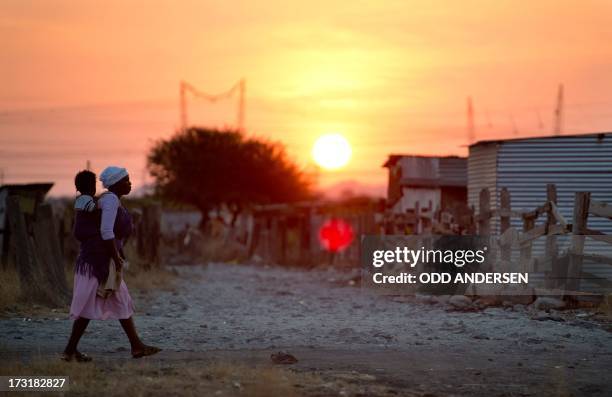 Woman carries her child as the sun sets in the shanty town of Nkaneng next to Lonmin's platinum smelter in Marikana on July 9, 2013. Police opened...