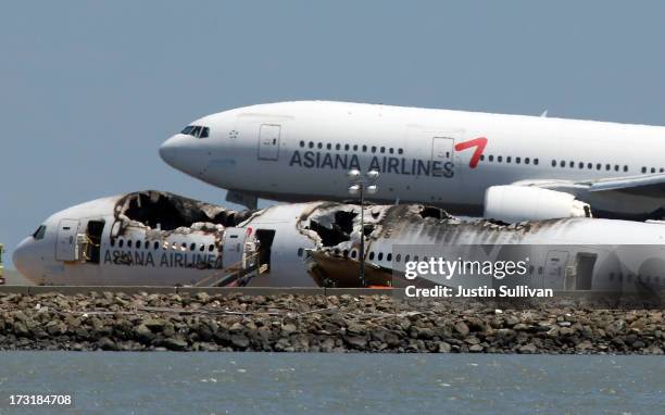 An Asiana Airlines flight lands next to the wreckage of Asiana Airlines flight 214 as it sits on runway 28L at San Francisco International Airport on...