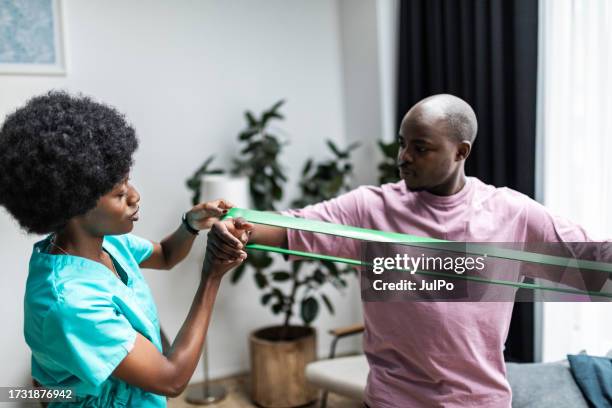 young black physiotherapist working with patient at home doing exercises with exercise band - patient identification band stock pictures, royalty-free photos & images