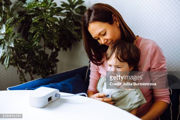 сute female child sits on woman knees while mother administers respiratory treatment using nebulizer - administers stock pictures, royalty-free photos & images